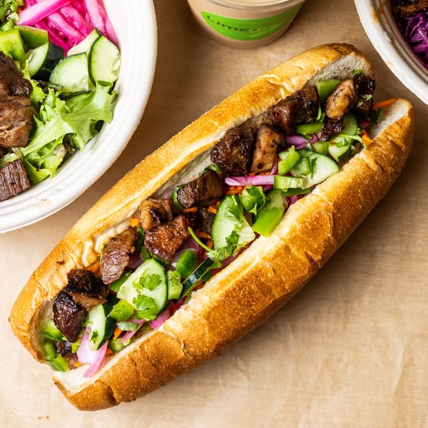 A banh mi sandwich with meat and vegetables, next to two bowls of food.