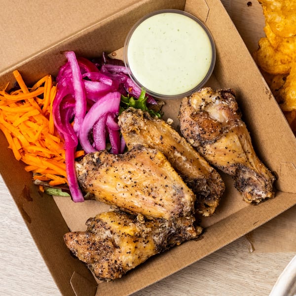 Crispy chicken wings with pickled red onions, shredded carrots, and a side of creamy green sauce.